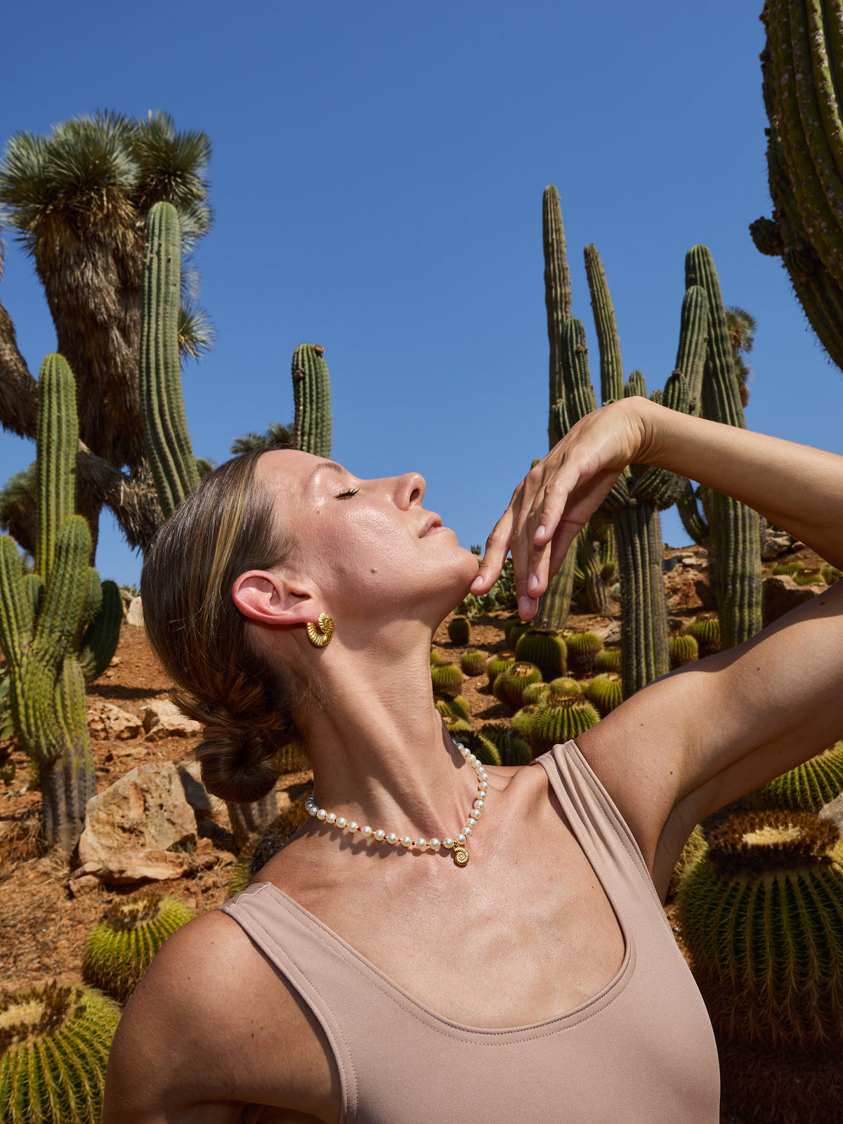 Model wearing the Ammonite and Pearls Necklace by Pola Jewellery — limited edition Majorica pearls necklace with gold vermeil ammonite pendant and red orange glass beads, Mallorca coastline.